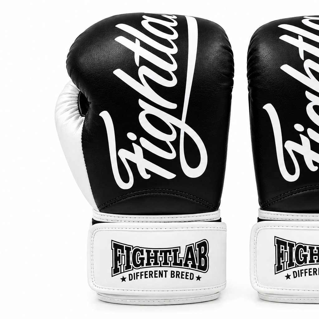 A pair of black and white boxing gloves with the brand name 'Fightlab' printed in white script on the black leather fronts and white wrist straps.