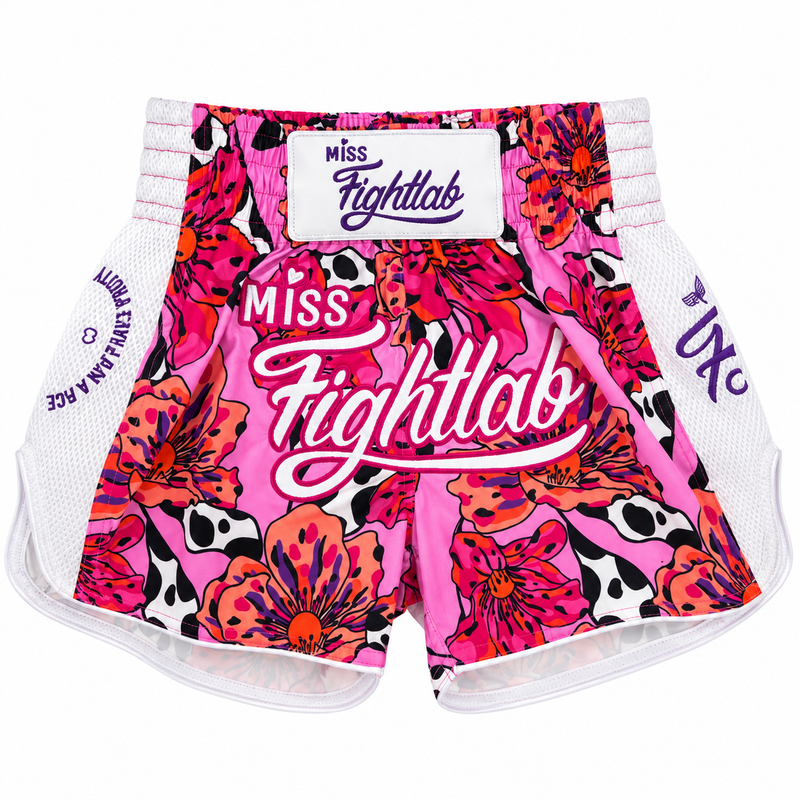 Pink and multicolor floral Miss Fightlab Muay Thai shorts with a white mesh side panel and a white waistband. The shorts feature a bold pattern of pink, orange, and black flowers, white cow print, and a large white 'Miss Fightlab' logo on the front.