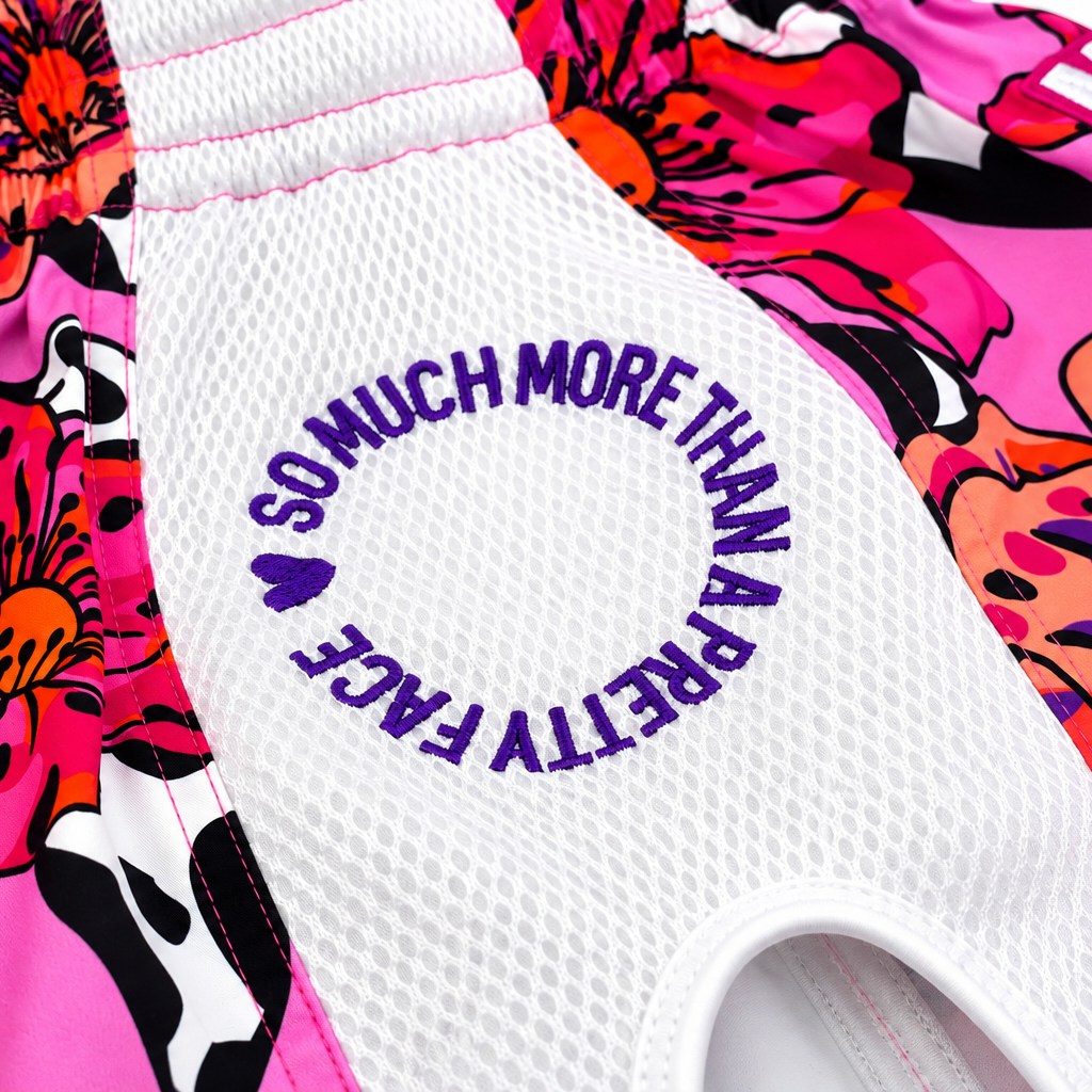 Close-up of Miss Fightlab Thai boxing shorts  with a white mesh center panel and a bright pink floral print in orange, purple, black, and white. Purple text on the white panel reads 'SO MUCH MORE THAN A PRETTY FACE'.