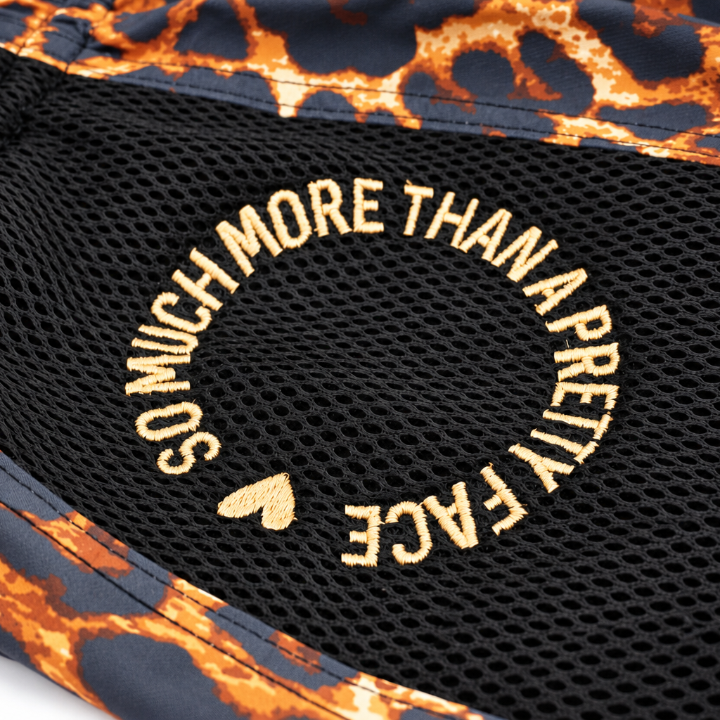 Close-up of a Miss Fightlab Leopard print shorts  with a leopard print border in orange, black, and gray, featuring a circular embroidered design that reads 'SO MUCH MORE THAN A PRETTY FACE' with a small heart.