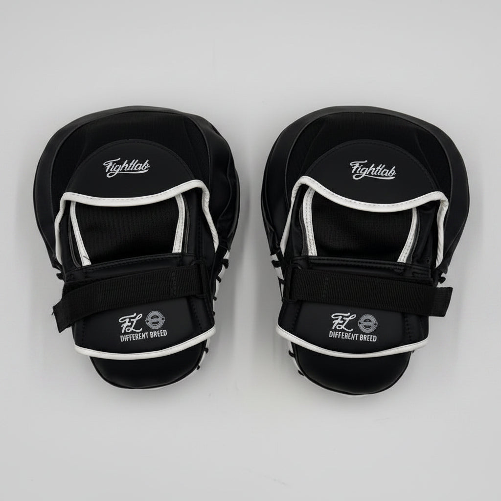 A pair of black boxing shin guards with white trim and adjustable velcro straps, displayed on a light gray background.