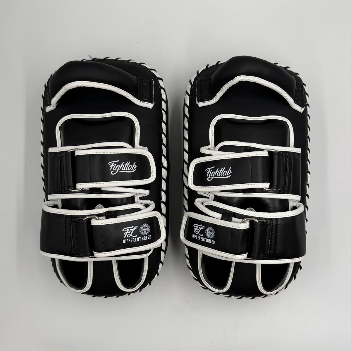 A pair of black and white martial arts striking pads on a light gray background. The pads feature multiple adjustable straps with white laces and white stitched borders.