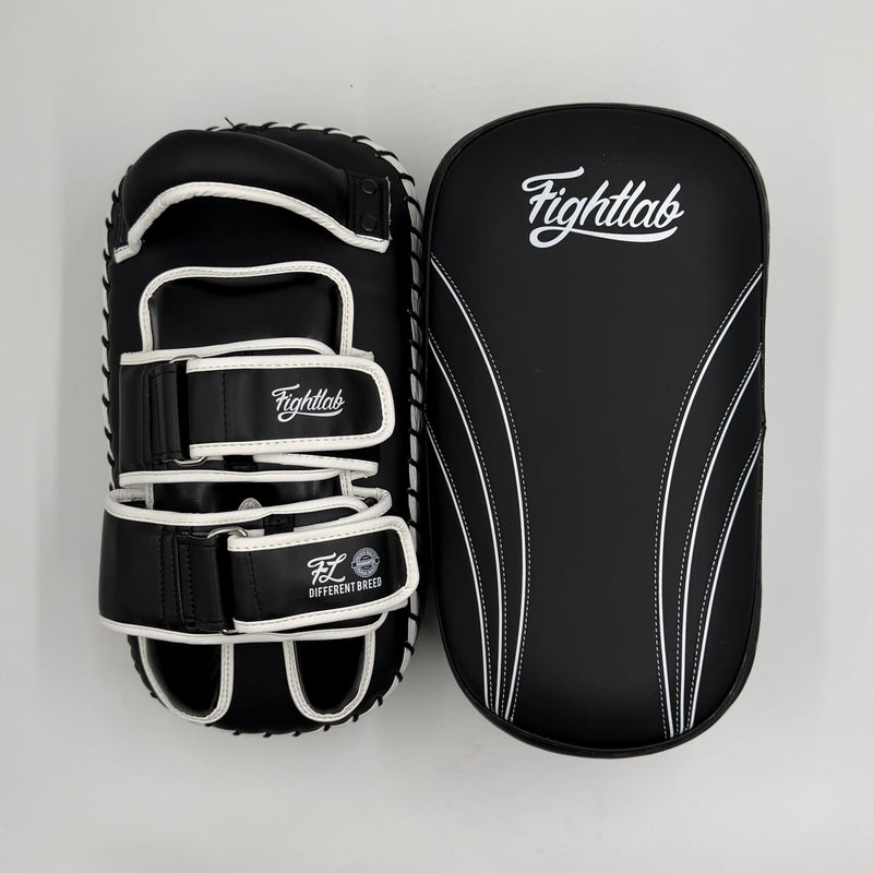 A pair of Fightlab martial arts striking pads, one open to show the adjustable hook-and-loop strap system and the other closed showing the padded surface with white stitching and the Fightlab logo, set against a plain light gray background.