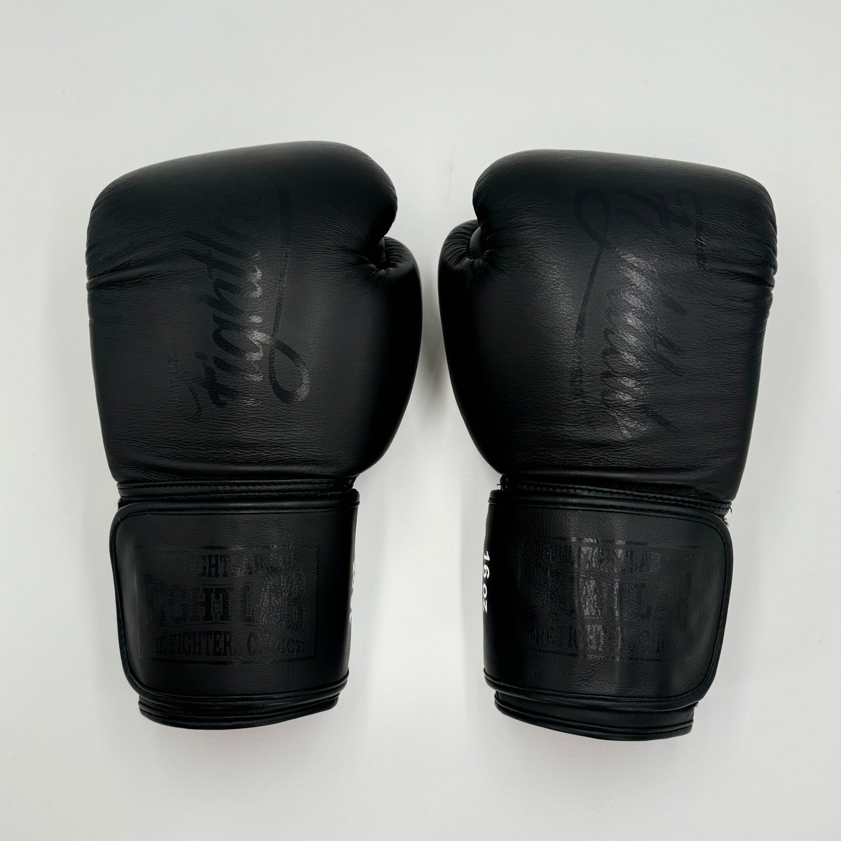 A pair of black leather boxing gloves with embossed branding, displayed side-by-side against a plain white background.